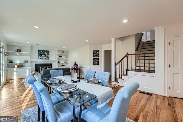 dining area featuring built in shelves, light wood-type flooring, and crown molding