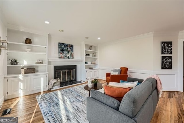 living room featuring built in shelves, light wood-type flooring, and ornamental molding