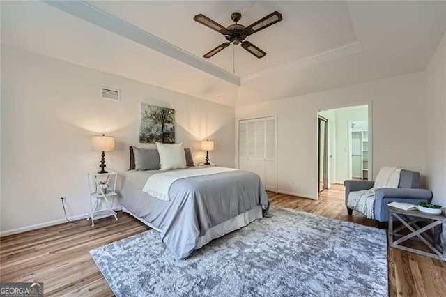 bedroom with ceiling fan, a raised ceiling, and wood-type flooring