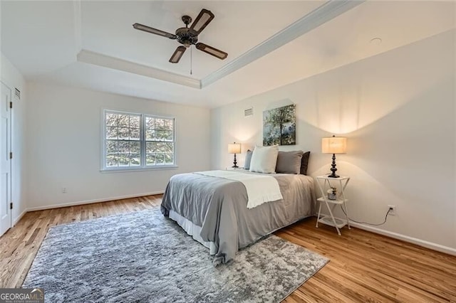 bedroom with ceiling fan, light hardwood / wood-style floors, and a tray ceiling