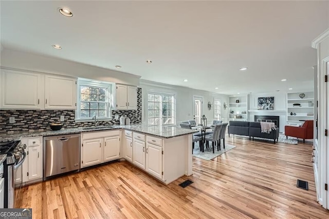 kitchen with kitchen peninsula, light stone counters, stainless steel appliances, light hardwood / wood-style flooring, and white cabinets