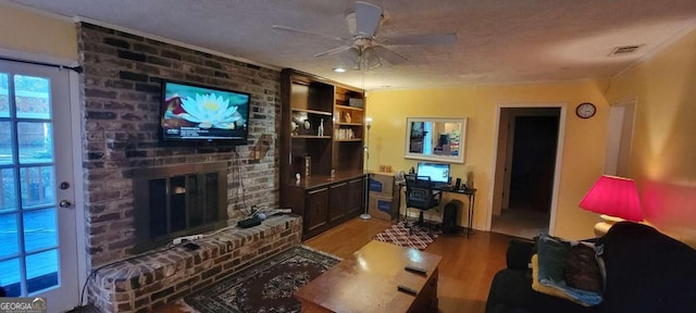 living room featuring light wood-type flooring, a textured ceiling, ceiling fan, built in features, and a fireplace