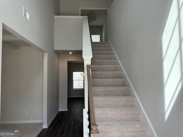 staircase featuring a towering ceiling, visible vents, baseboards, and wood finished floors