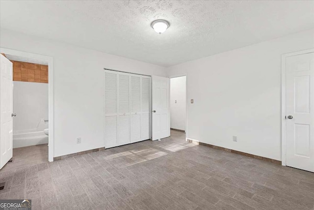 unfurnished bedroom with ensuite bathroom, a closet, light hardwood / wood-style floors, and a textured ceiling