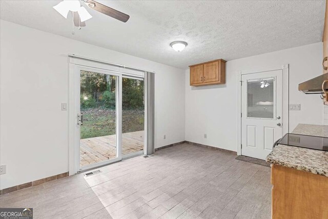 unfurnished dining area with ceiling fan, light hardwood / wood-style floors, and a textured ceiling