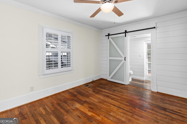 unfurnished bedroom with a barn door, ceiling fan, dark hardwood / wood-style flooring, and ornamental molding