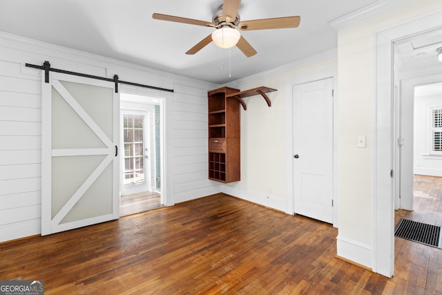 unfurnished bedroom featuring ceiling fan, a barn door, crown molding, and dark wood-type flooring