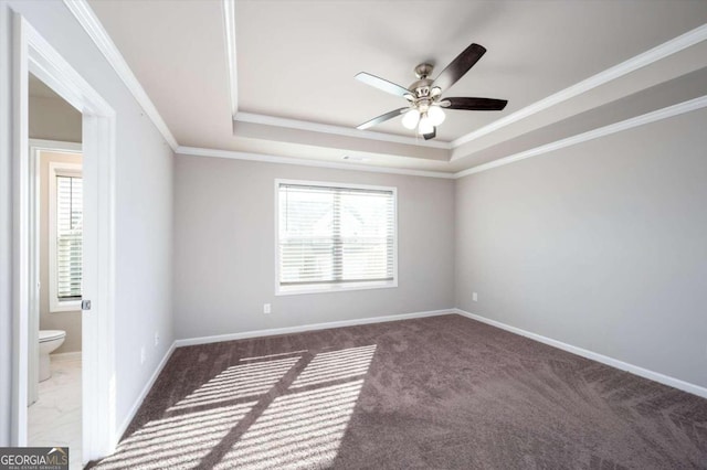 unfurnished room featuring a tray ceiling, ceiling fan, ornamental molding, and dark colored carpet