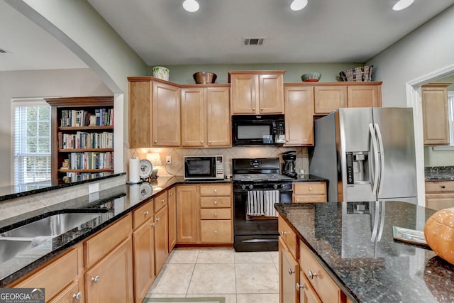 kitchen with dark stone counters, black appliances, sink, light tile patterned floors, and tasteful backsplash