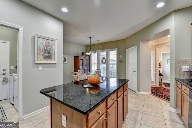 kitchen with washer and dryer, pendant lighting, dark stone countertops, a chandelier, and a center island