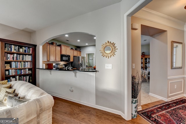 kitchen with a kitchen breakfast bar, kitchen peninsula, light hardwood / wood-style flooring, ornamental molding, and stainless steel fridge with ice dispenser