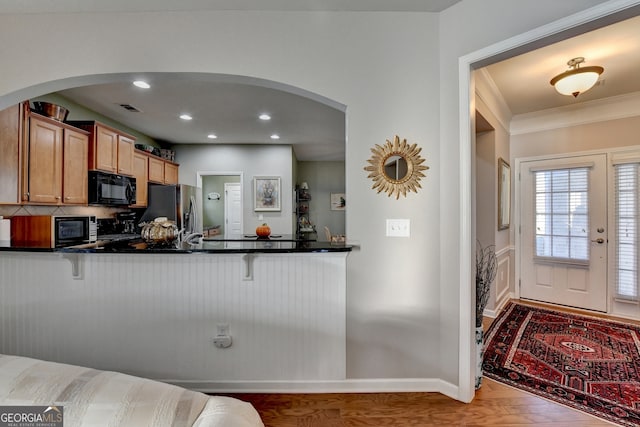 kitchen featuring crown molding, hardwood / wood-style flooring, stainless steel fridge, kitchen peninsula, and a breakfast bar area