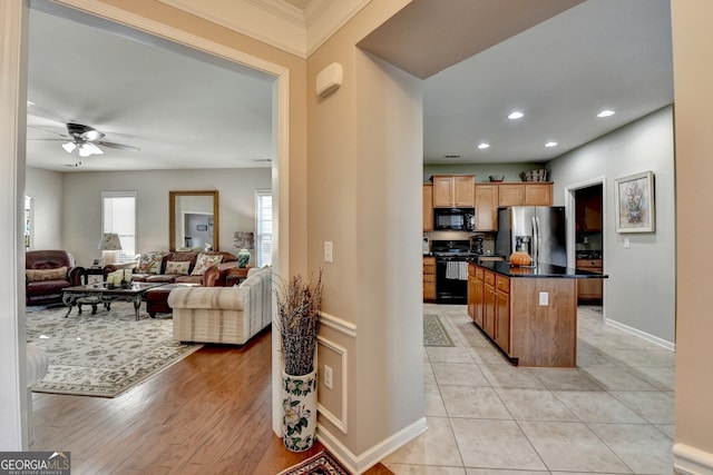 kitchen featuring ceiling fan, light hardwood / wood-style floors, a kitchen island, black appliances, and ornamental molding