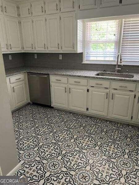 kitchen featuring decorative backsplash, white cabinetry, sink, and stainless steel dishwasher