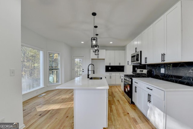 kitchen featuring stainless steel appliances, sink, a center island with sink, light hardwood / wood-style flooring, and white cabinetry