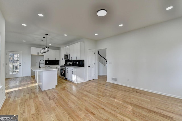 kitchen with white cabinetry, an island with sink, light hardwood / wood-style floors, pendant lighting, and appliances with stainless steel finishes