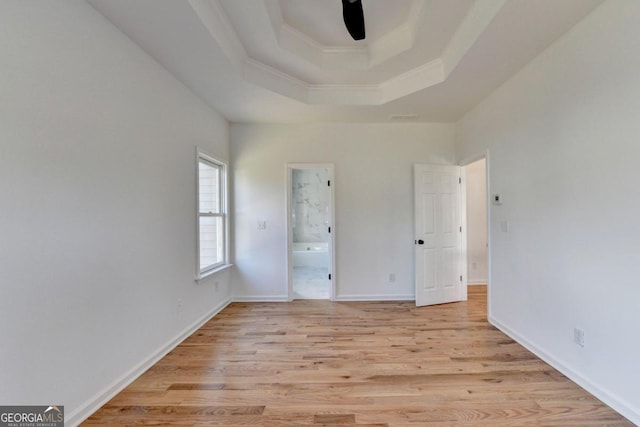 unfurnished bedroom with crown molding, ensuite bath, light hardwood / wood-style flooring, ceiling fan, and a tray ceiling