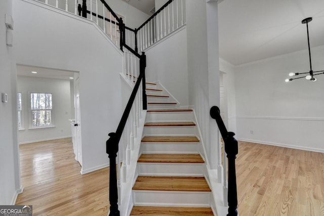 stairway featuring a notable chandelier, hardwood / wood-style floors, a high ceiling, and ornamental molding