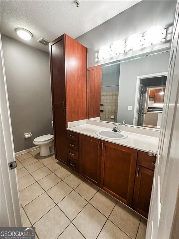 bathroom featuring tile patterned flooring, vanity, a textured ceiling, and toilet