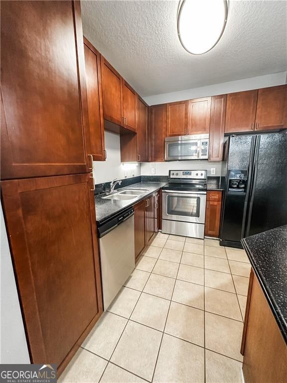 kitchen with sink, dark stone countertops, a textured ceiling, light tile patterned flooring, and appliances with stainless steel finishes