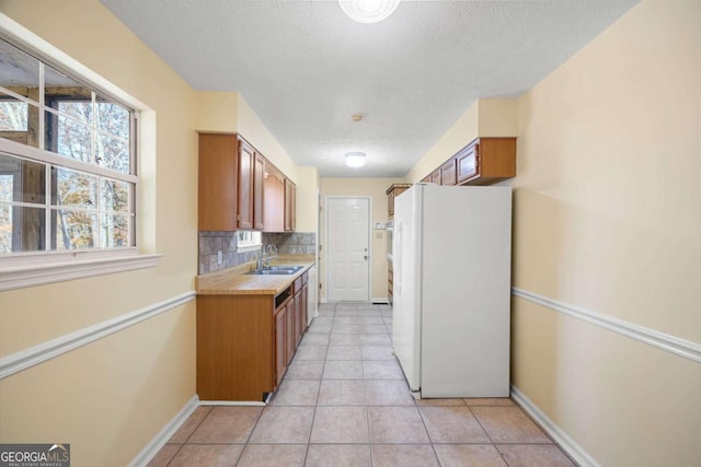 kitchen featuring white refrigerator, sink, decorative backsplash, light tile patterned floors, and a textured ceiling