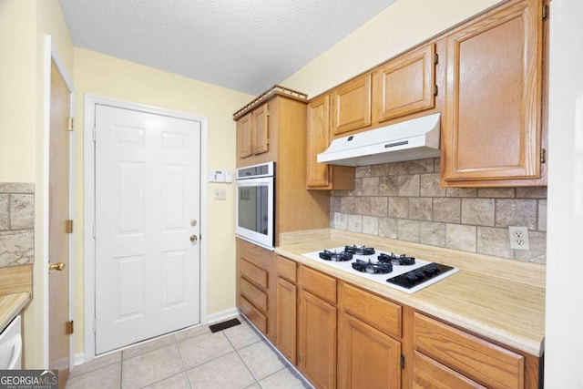 kitchen featuring stainless steel oven, white gas cooktop, backsplash, a textured ceiling, and light tile patterned flooring