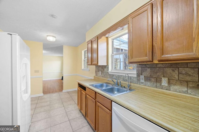 kitchen featuring white appliances, backsplash, sink, light tile patterned floors, and a textured ceiling