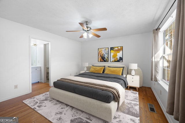 bedroom with connected bathroom, multiple windows, and wood-type flooring