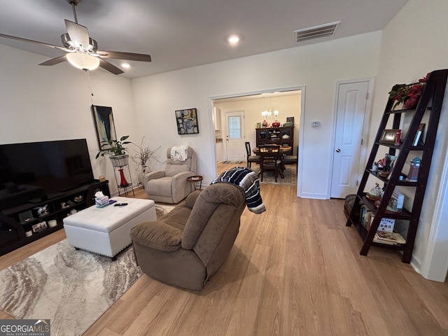 living room featuring ceiling fan with notable chandelier and light wood-type flooring