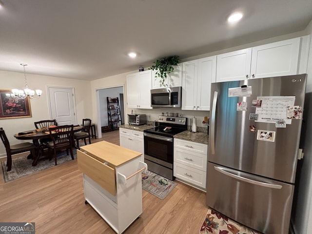 kitchen with an inviting chandelier, white cabinets, hanging light fixtures, light wood-type flooring, and appliances with stainless steel finishes