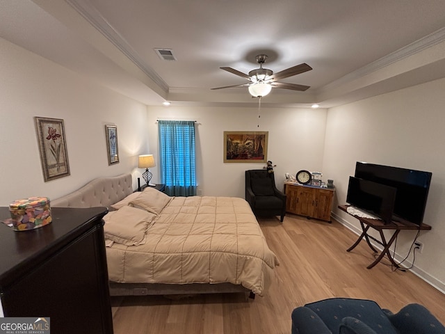 bedroom featuring ceiling fan, a raised ceiling, ornamental molding, and light hardwood / wood-style flooring