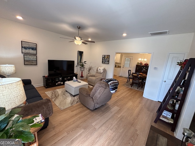 living room featuring ceiling fan with notable chandelier and light hardwood / wood-style flooring