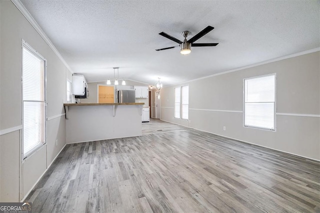 unfurnished living room with lofted ceiling, ceiling fan with notable chandelier, light wood-type flooring, a textured ceiling, and ornamental molding