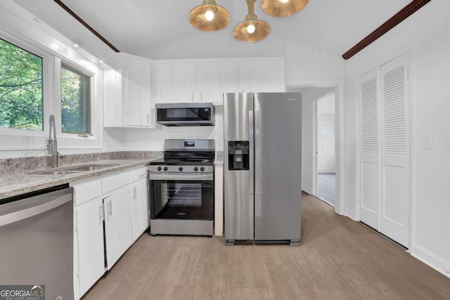 kitchen featuring stainless steel appliances, white cabinetry, pendant lighting, and vaulted ceiling