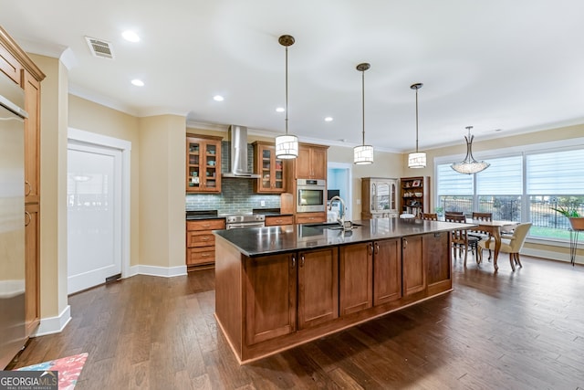 kitchen featuring wall chimney range hood, sink, hanging light fixtures, an island with sink, and dark hardwood / wood-style flooring