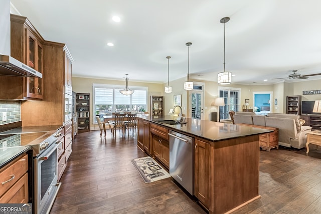 kitchen with sink, dark wood-type flooring, stainless steel appliances, pendant lighting, and a center island with sink