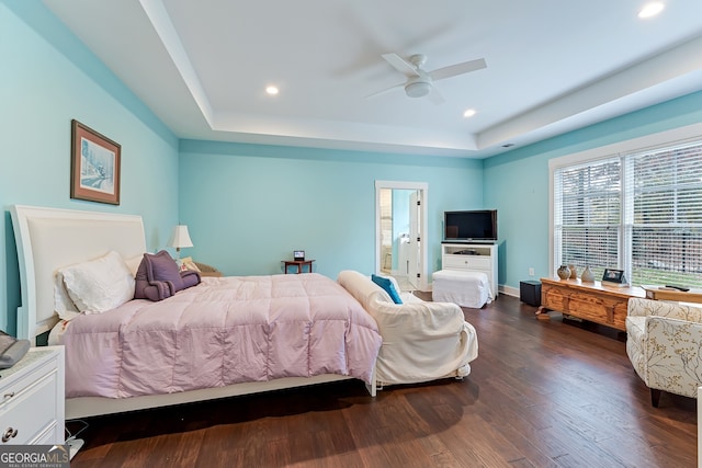 bedroom featuring a raised ceiling, ensuite bath, ceiling fan, and dark wood-type flooring