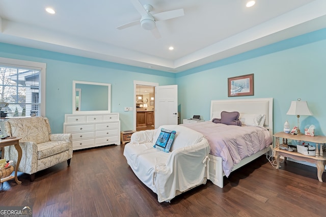 bedroom with a raised ceiling, ensuite bath, ceiling fan, and dark wood-type flooring