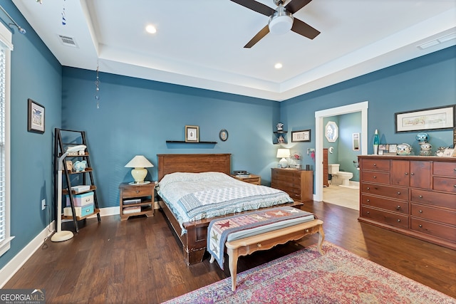 bedroom with ceiling fan, ensuite bathroom, dark wood-type flooring, and a tray ceiling