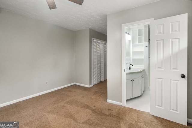 unfurnished bedroom featuring sink, ceiling fan, a textured ceiling, light colored carpet, and a closet