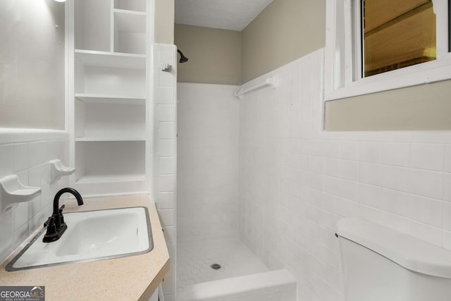 bathroom featuring a tile shower, vanity, toilet, and tile walls