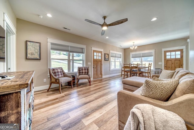 living room featuring ceiling fan with notable chandelier and light wood-type flooring