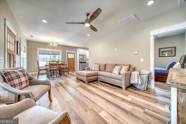 living room featuring ceiling fan with notable chandelier and light hardwood / wood-style floors