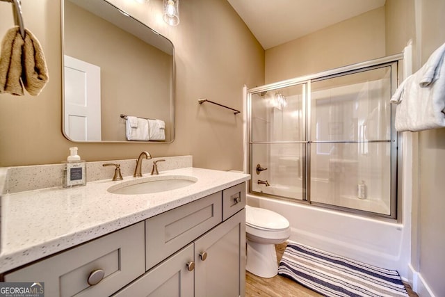 full bathroom featuring combined bath / shower with glass door, vanity, hardwood / wood-style flooring, and toilet