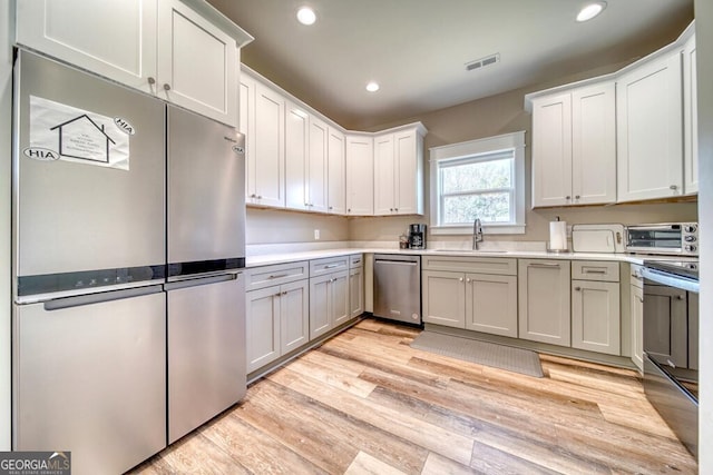 kitchen with white cabinets, sink, light wood-type flooring, and stainless steel appliances