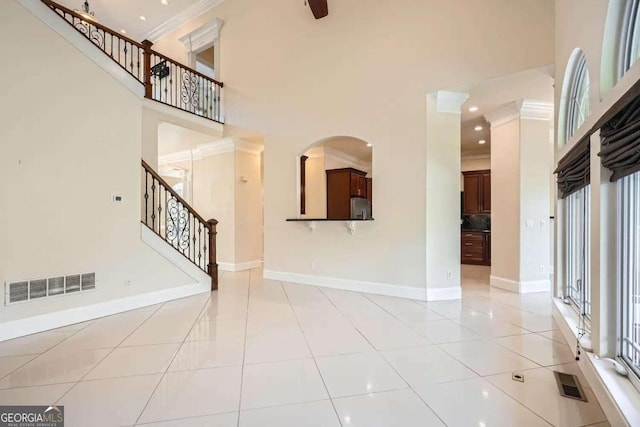 unfurnished living room with crown molding, light tile patterned floors, and a high ceiling