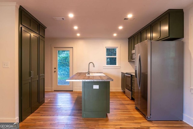 kitchen with appliances with stainless steel finishes, a kitchen island with sink, crown molding, sink, and light hardwood / wood-style floors