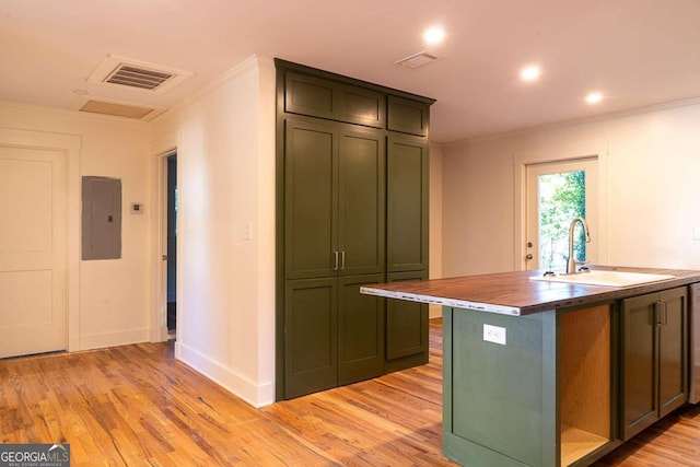 kitchen with light wood-type flooring, crown molding, sink, electric panel, and an island with sink