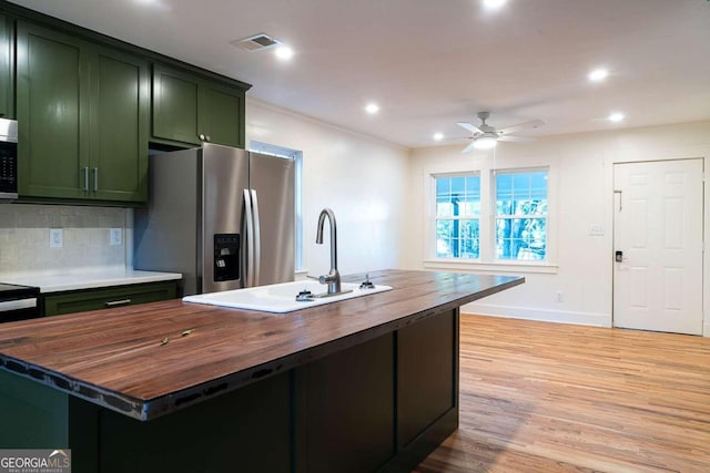 kitchen with sink, green cabinetry, butcher block countertops, light hardwood / wood-style floors, and stainless steel appliances