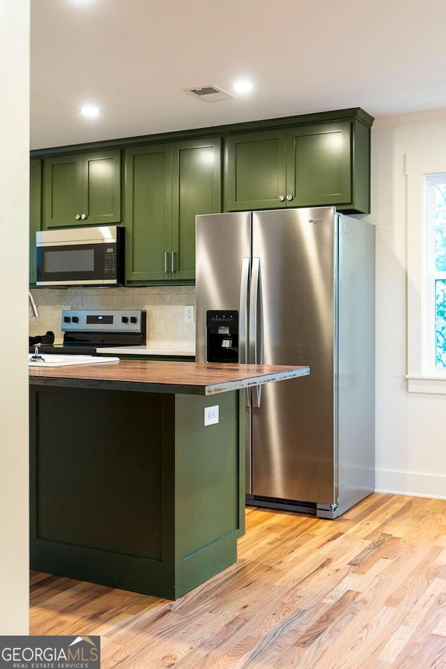 kitchen with decorative backsplash, appliances with stainless steel finishes, light hardwood / wood-style floors, and green cabinetry